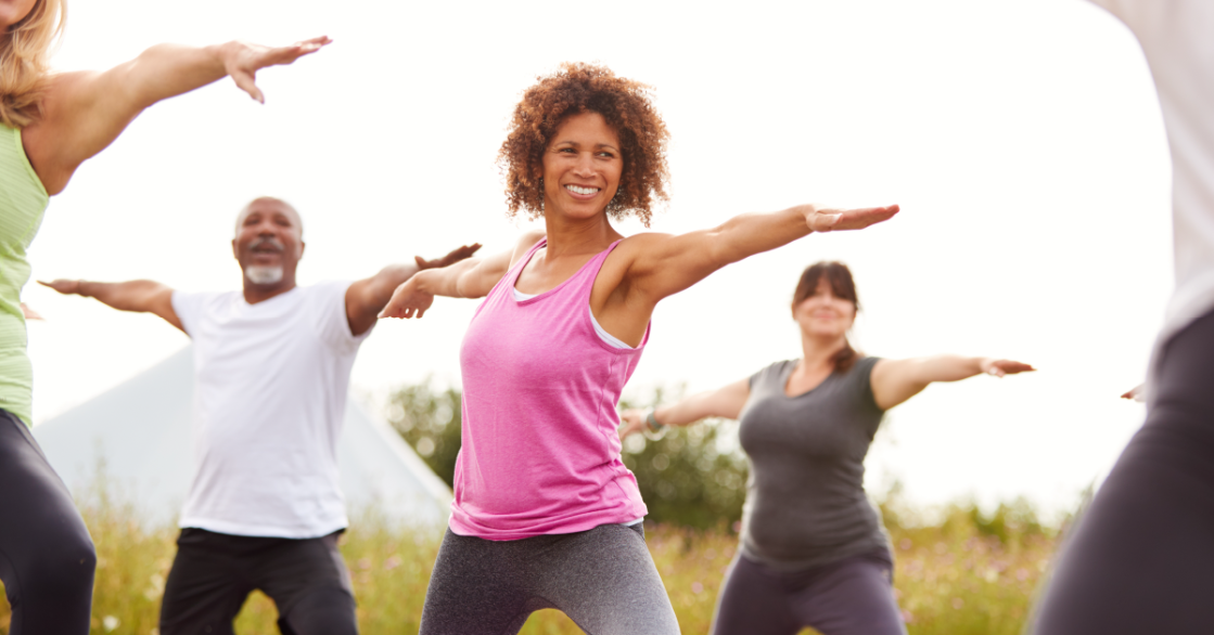 A group of adults practices yoga outside to relieve their stress.