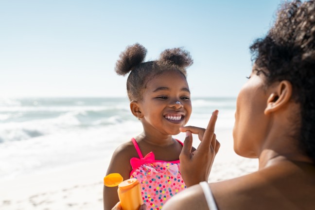 Mom putting sunscreen on her daughter at the beach