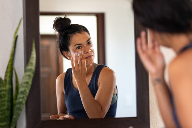 Woman looking in the mirror and applying skin cream